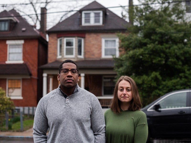 Maddie Gioffre (right) and Shaquille Charles stand in front of their Wilkinsburg home on April 5, 2022. The two purchased the home in early 2020 and were promptly subjected to an assessment appeal. They are the lead plaintiffs in a lawsuit challenging the way Allegheny County calculates property assessments after appeals. (Photo by Lindsay Dill/PublicSource)