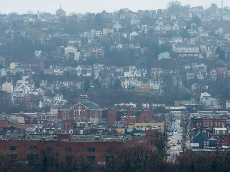 Mist blurs the patchwork housing of the South Side Slopes during a dark afternoon on Tuesday, July 6, 2022, as seen from across the Monongahela River. (Photo by Stephanie Strasburg/PublicSource)