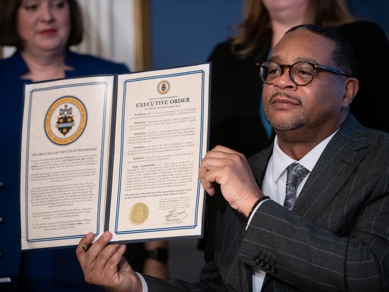 Pittsburgh Mayor Ed Gainey holds up an executive order addressing non-profit tax-exempt property after signing it in his City-County Building offices on Tuesday, Jan. 24, 2023, in Downtown. Behind him is Krysia M. Kubiak, chief legal officer and city solicitor, left, and Jen Gula, director of finance and treasurer for the city. (Photo by Stephanie Strasburg/PublicSource)