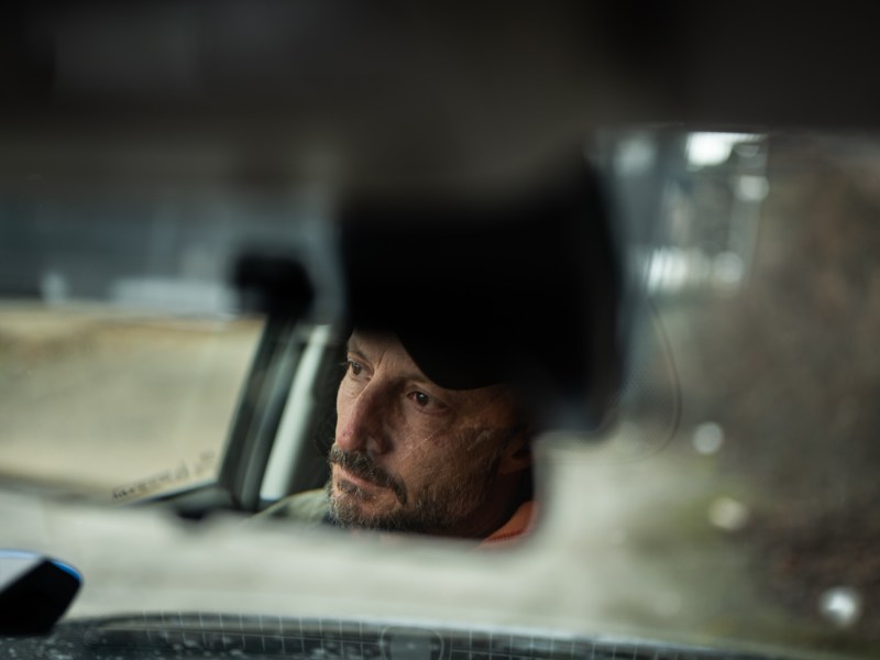 David Lettrich, executive director of Bridge to the Mountains, is reflected in his car mirror as he takes calls from outreach workers in between rounds to encampments throughout the city on Jan. 26, 2023. (Photo by Stephanie Strasburg/PublicSource)