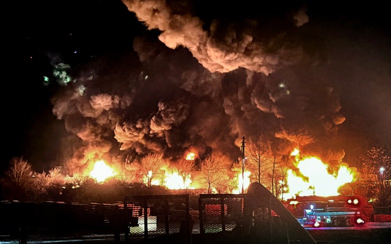 A fire burns above a train wreck at night.