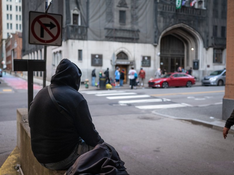 A person waits across the street for the Smithfield United Church of Christ shelter to open for the evening on May 8, 2023, in downtown Pittsburgh. (Photo by Stephanie Strasburg/PublicSource)