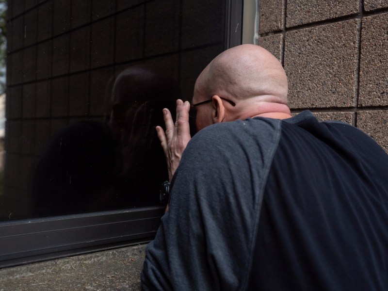 Eric Miskovitch, seen from behind in a black and grey shirt, looks through a window of the former State Correctional Institution Pittsburgh on Thursday, May 18, 2023, in Marshall-Shadeland. Miskovitch used to be incarcerated at the institution, and he’s now pitching that the vacant building could be part of the solution to the housing crisis. (Photo by Stephanie Strasburg/PublicSource)