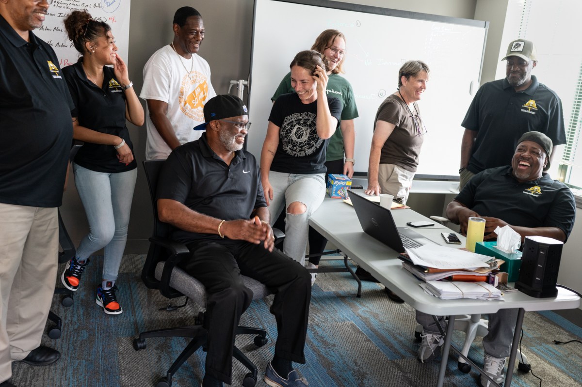 Richard Garland, center, seated, executive director of Reimagine Reentry, laughs with his team on Thursday, Sept. 7, 2023, in their Hill District offices. Garland and his team work to identify trends in community violence and to prevent violence through victim relocation, connecting to services and supports and creating community relationships. (Photo by Stephanie Strasburg/PublicSource)