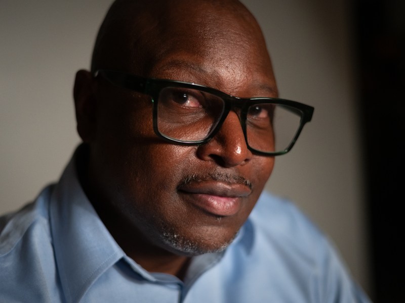 George McClure sits for a portrait. He is wearing a blue-collared shirt and black-rimmed glasses.