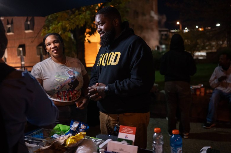 Tanisha Long, left, is wearing a graphic T-shirt. MAN-E is wearing a black hoodie with yellow text that says, "1Hood." Both are talking to people outside the Allegheny County Jail. 