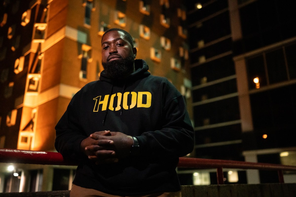 A man in a 1Hood hoodie stands in front of a jail