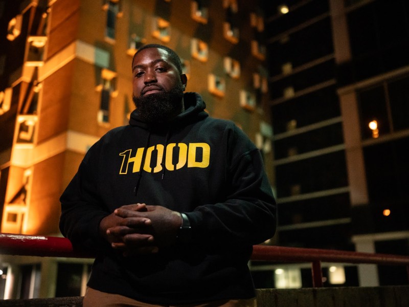 A man in a 1Hood hoodie stands in front of a jail