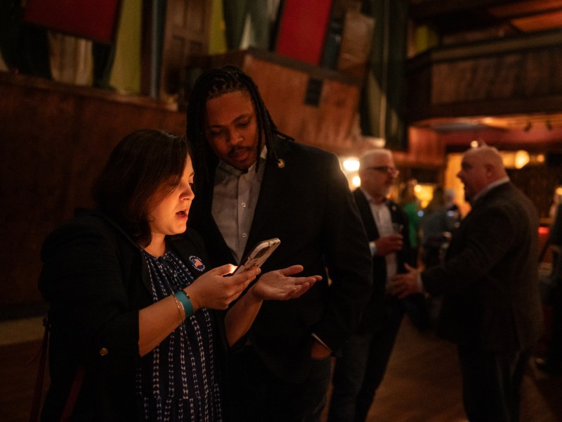 Emma Shoucair, left, attorney for the Allegheny County Democratic Committee, looks at the first poll numbers in for the night with state Rep. Malcolm Kenyatta at the election night party for Sara Innamorato, Democratic nominee for Allegheny County Executive, at Mr. Smalls in Millvale. “It was mostly quiet,” Shoucair said. There were a couple of fist fights, but mostly over school board races.” (Photo by Stephanie Strasburg/PublicSource)