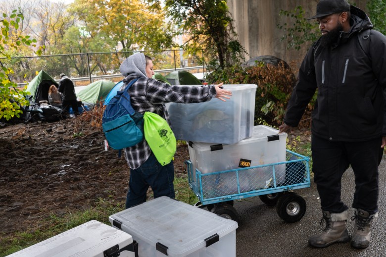 Lia S., who declined to share her last name, and Muhammad Ali Nasir, also known by his emcee name MAN-E, the advocacy & policy, civic engagement coordinator for 1Hood and founder of Community Care & Resistance In Pittsburgh (CCRIP), unload tubs of supplies for people living outside on a rainy Sunday, Oct. 29, 2023, in Downtown Pittsburgh. The CCRIP team has remained busy since they started their street outreach about a year prior in response to the shutdown of the Stockton Avenue encampment on the North Side. (Photo by Stephanie Strasburg/PublicSource)