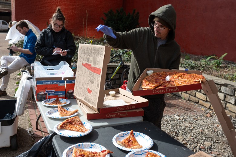 Russell Beyer, a volunteer with Community Care & Resistance In Pittsburgh (CCRIP), serves up pizza and coffee for people getting evicted from the site of an encampment along First Avenue by Boulevard of the Allies, on Wednesday morning, Nov. 8, 2023, in downtown Pittsburgh. Beyer lives at Second Avenue Commons, where he’s watched newly unhoused people come through and get turned away for lack of room. “There's no capacity. So they sit outside, and whatever they have with whatever they have in their hands. As a newly homeless person, there is, there's nowhere to go. And that is troubling to me,” he said. (Photo by Stephanie Strasburg/PublicSource)