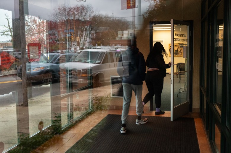 People enter the waiting area for District Judge Oscar Petite’s courtroom as seen through reflections in the vestibule glass, Wednesday, Nov. 22, 2023, in the Hill District. (Photo by Stephanie Strasburg/PublicSource)