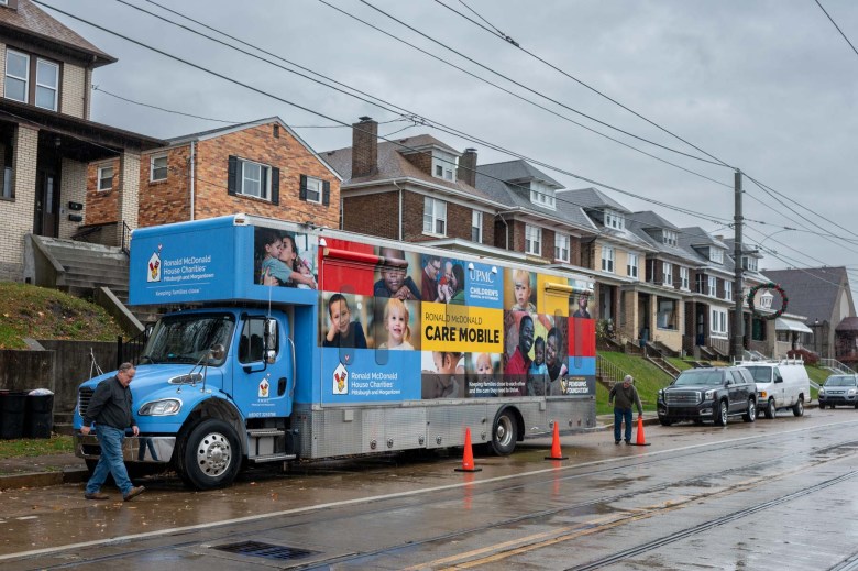 A blue truck marked with the words "Care Mobile" parked on a wet street.