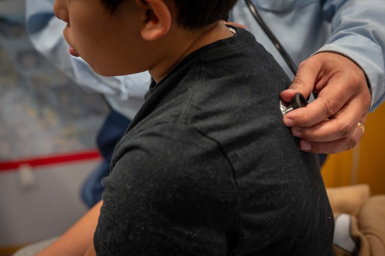 A young boy with a stethoscope pressed to his back.