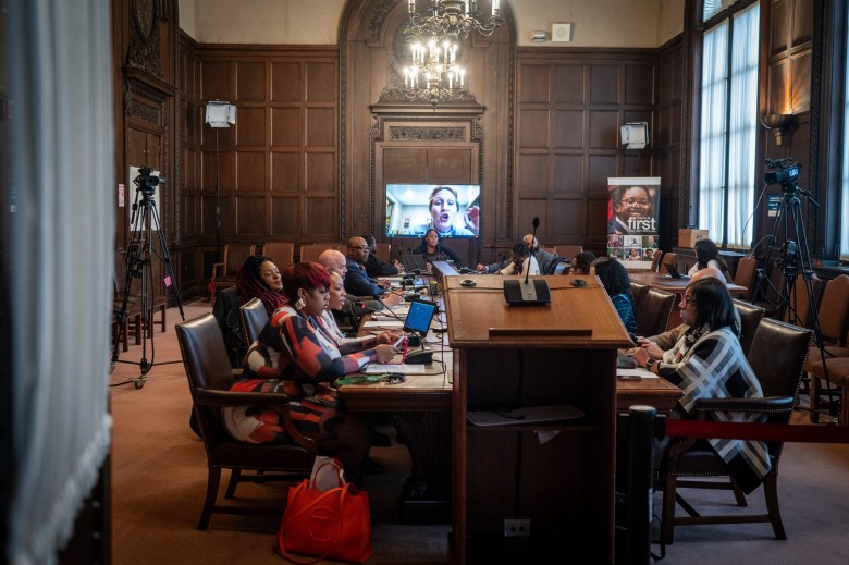 A group of people sitting at a table as a person talks to them via video.