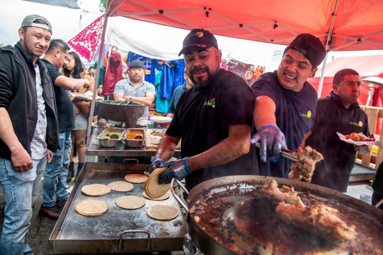 People cooking tacos on an outdoor grill.