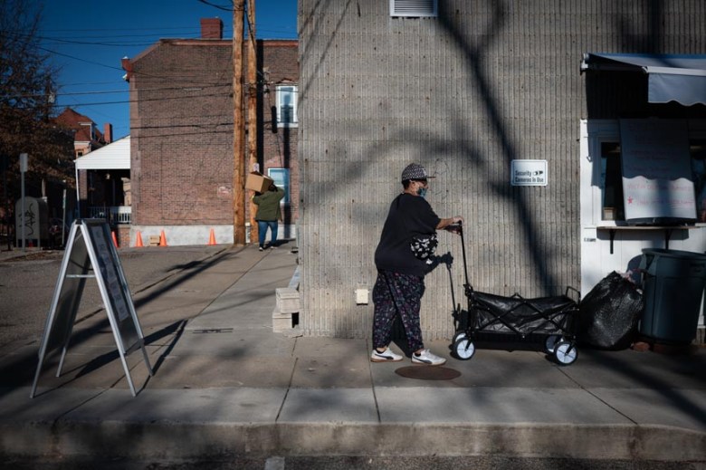 A woman volunteer at the Oakland Food Pantry pushes a food cart down the sidewalk.