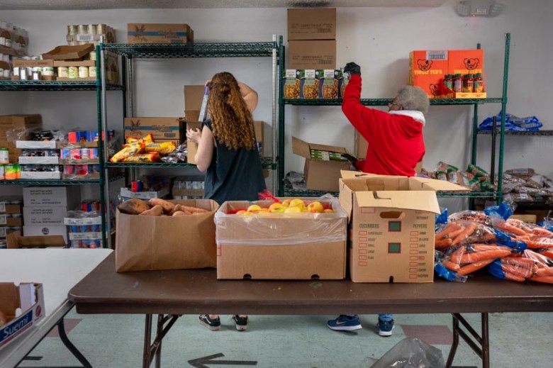 Two women volunteers stock shelves of food at the Oakland Food Pantry.