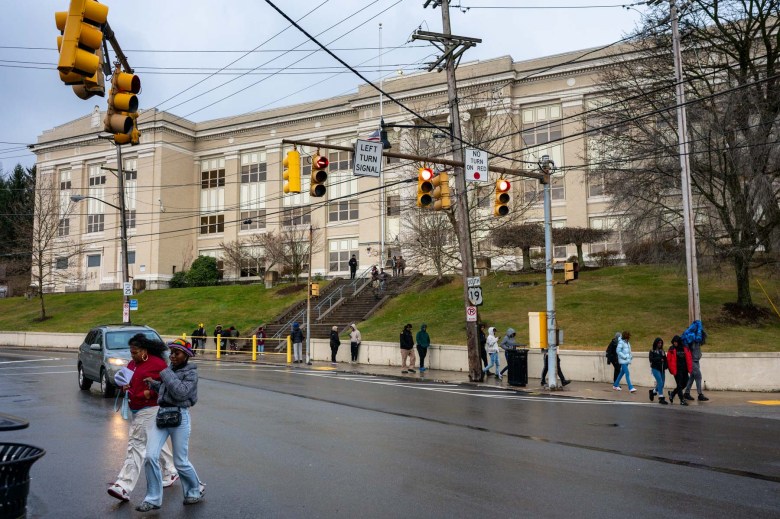 A group of kids crossing the street in front of a school building.