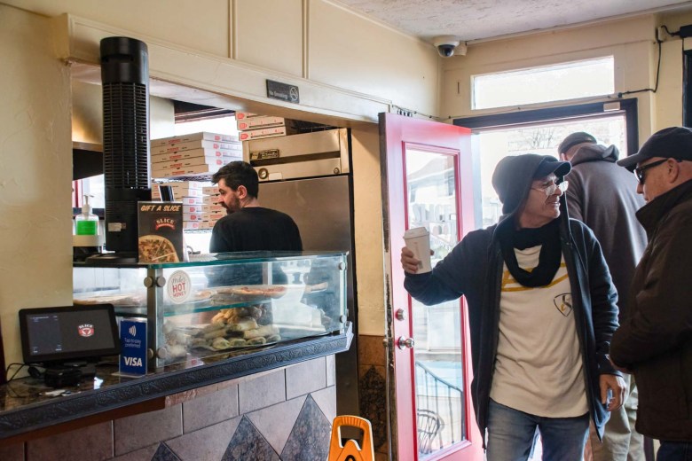 A group of people standing in a pizza shop.