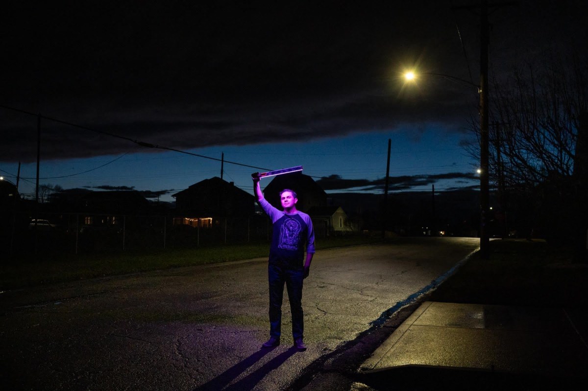 A man holding a purple light in the street at night.