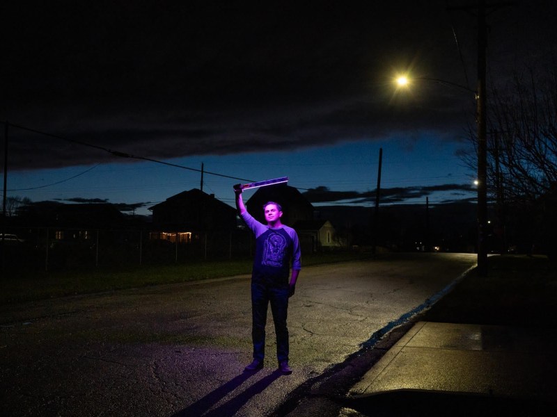 A man holding a purple light in the street at night.