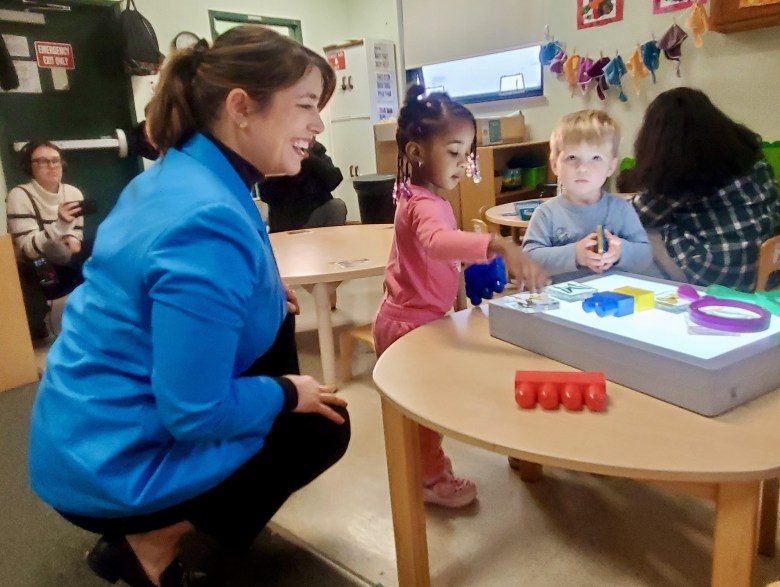 a woman in a blue coat plays with children around a table