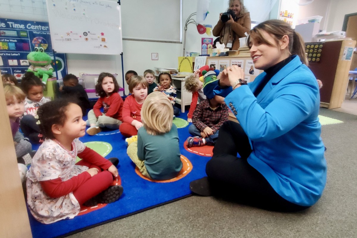 A woman in a blue jacket is sitting on the floor in front of a group of children.