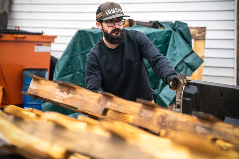 A man with a beard and glasses lifts a wooden pallet 