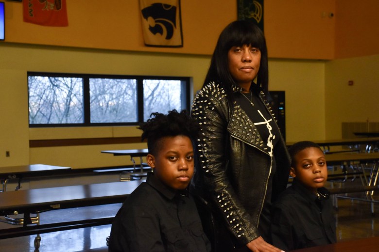 A woman and two boys standing at a table in a classroom.