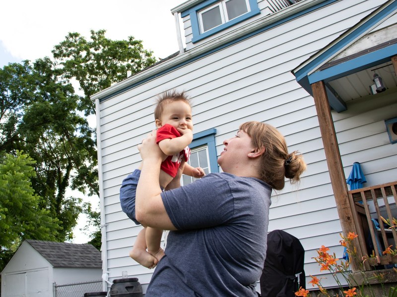 A woman with red hair in a blue T-shirt looks at her son as she holds him in her backyard.