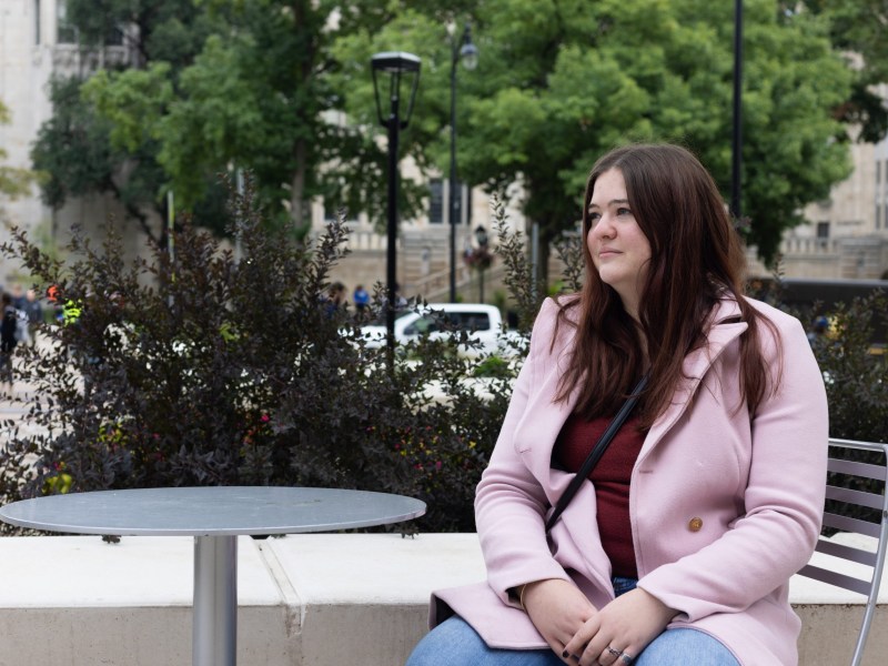 Kaleigh Mauroni sits at a small table next to the Cathedral of Learning while looking to her right. .