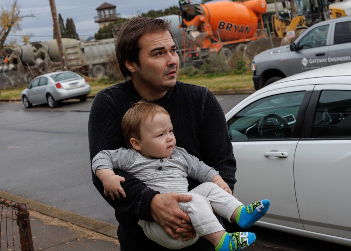 A man holding a baby in front of a concrete site.