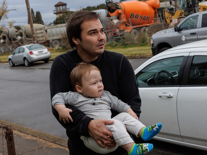 A man holding a baby in front of a concrete site.