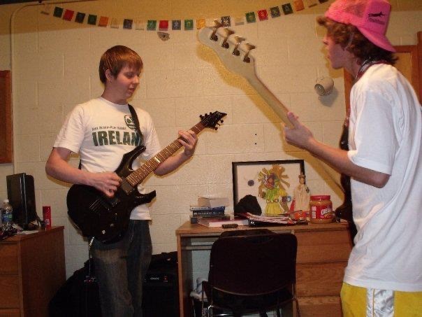 Two young men playing guitar in a dorm room.