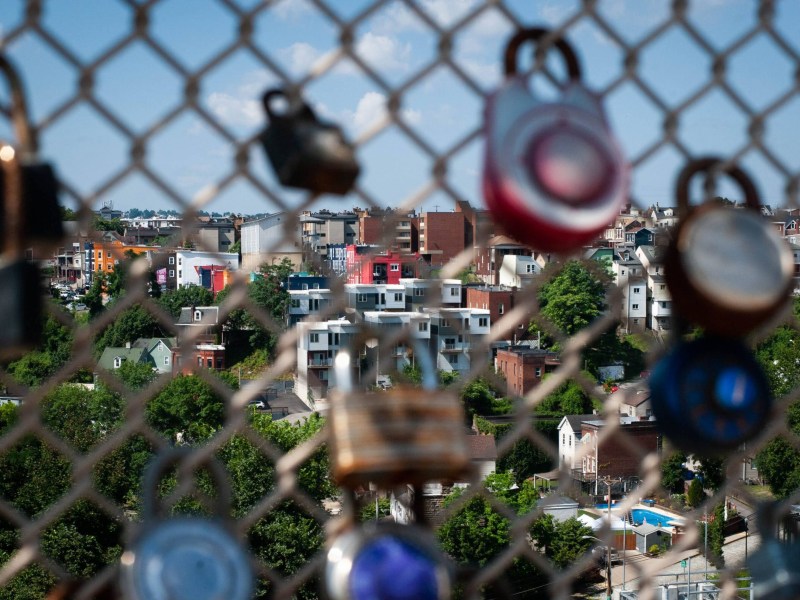 The apartments and homes of Central Oakland are seen beyond padlocks hanging on the Schenley Bridge, on Wednesday, July 20, 2022. (Photo by Stephanie Strasburg/Public Source)