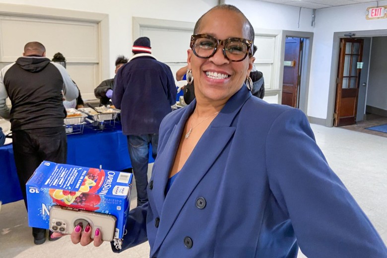 A woman holding a box of Capri Sun juice pouches and a phone in front of a group of people at a table.