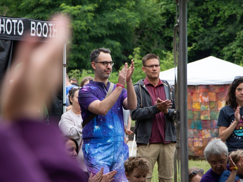 Todd Feiler wears a galaxy-style romper and claps for a performance with a group of people.